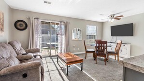 A living room with a sofa, a coffee table, and a dining area with chairs and a TV. - Windsor Cottage Fall Creek Beauty by Table Rock! (Branson)
