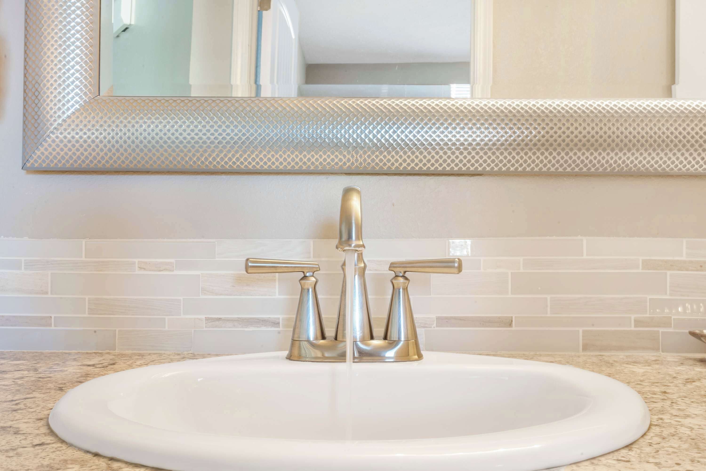 A bathroom with a white sink, two gold faucets, and a mirror with a textured frame.