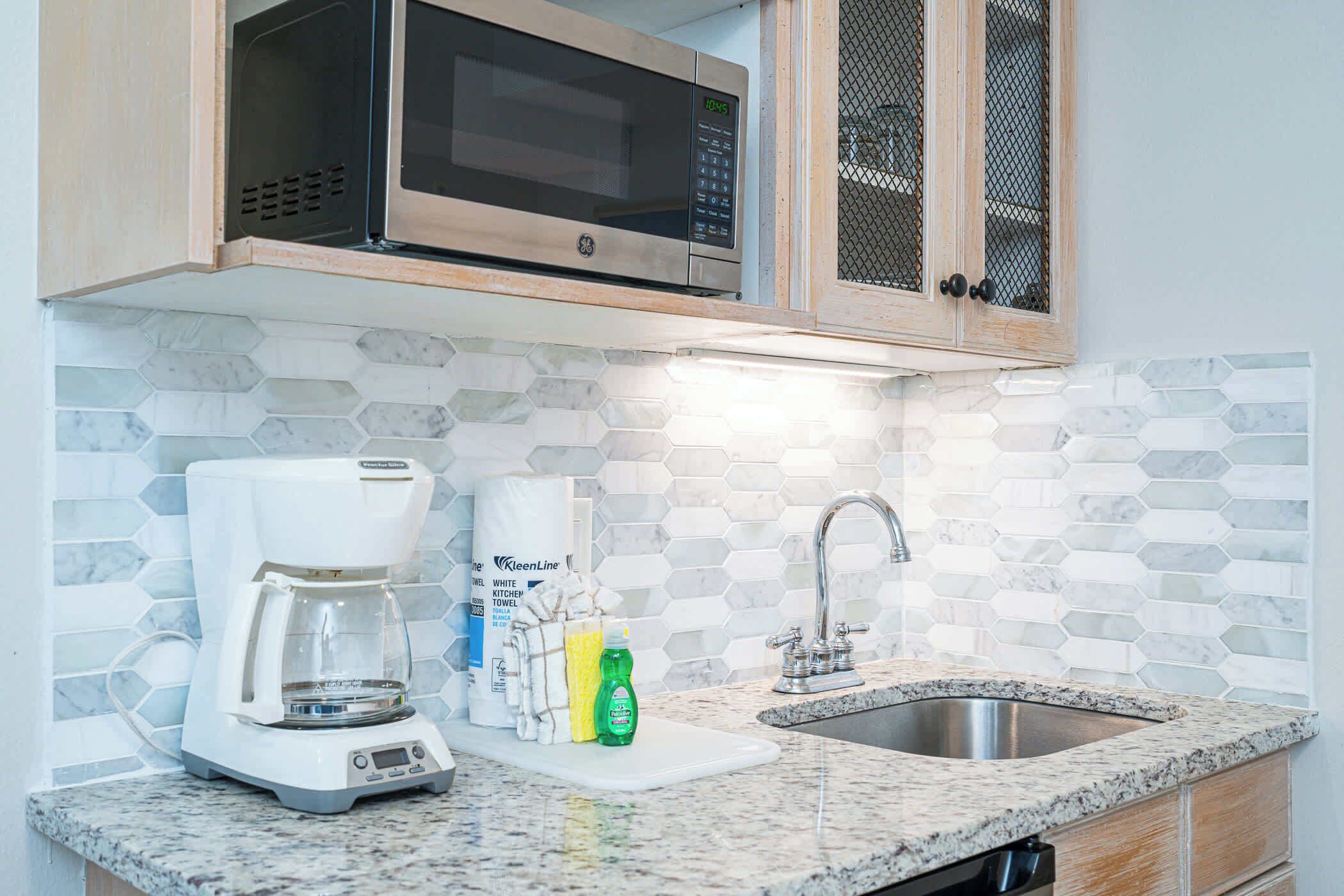 A kitchen with a microwave, coffee maker, sink, and a tiled backsplash.
