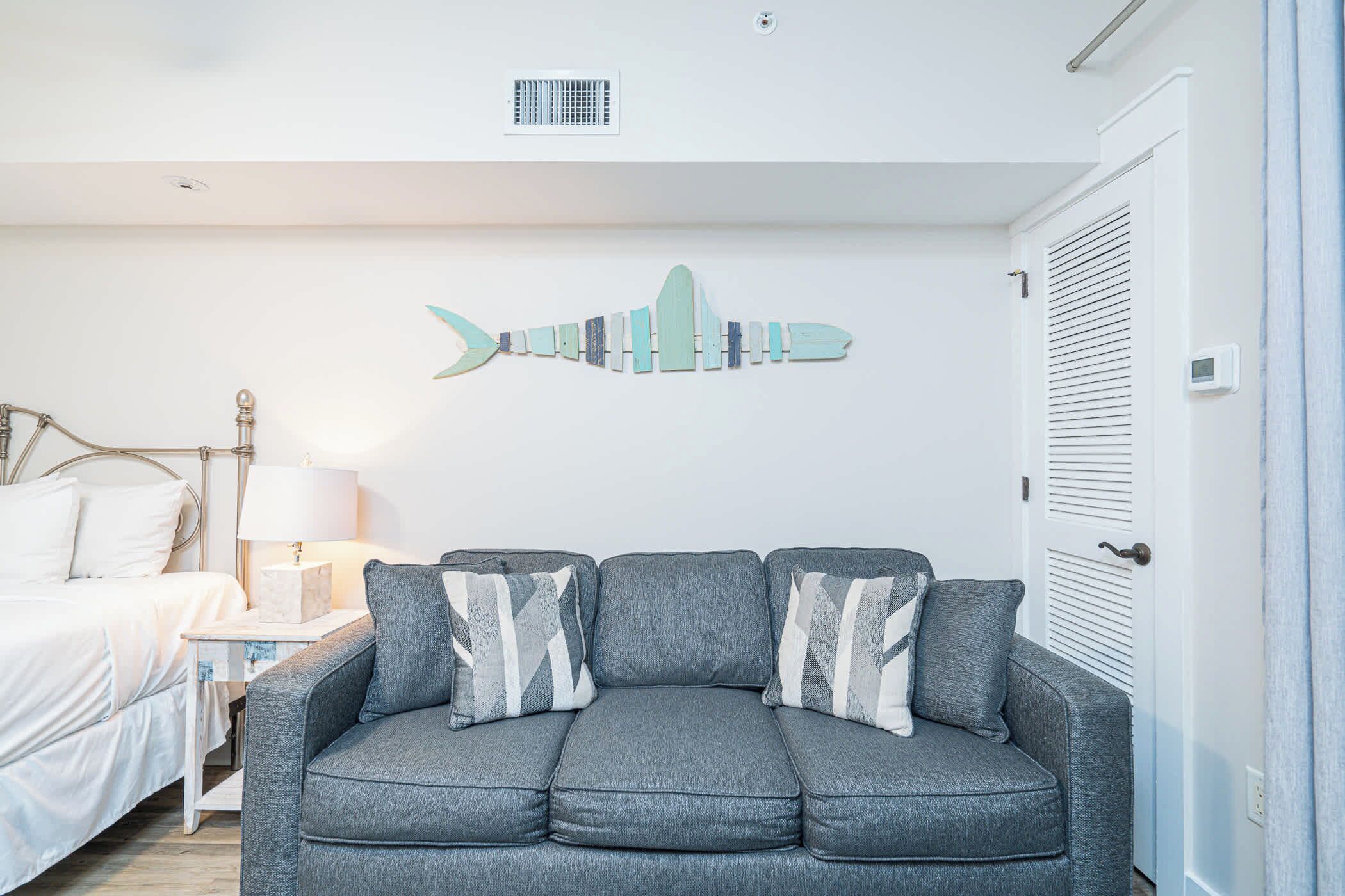Een moderne slaapkamer met een grijze bank, een bed, een nachtkastje en een wanddecoratie.