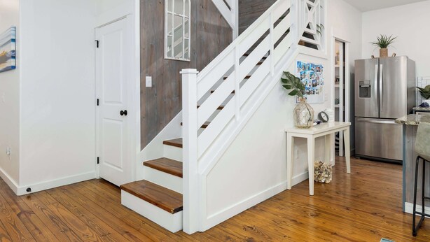 Una cocina moderna con refrigerador de acero inoxidable, piso de madera y escalera blanca con detalles de madera.
