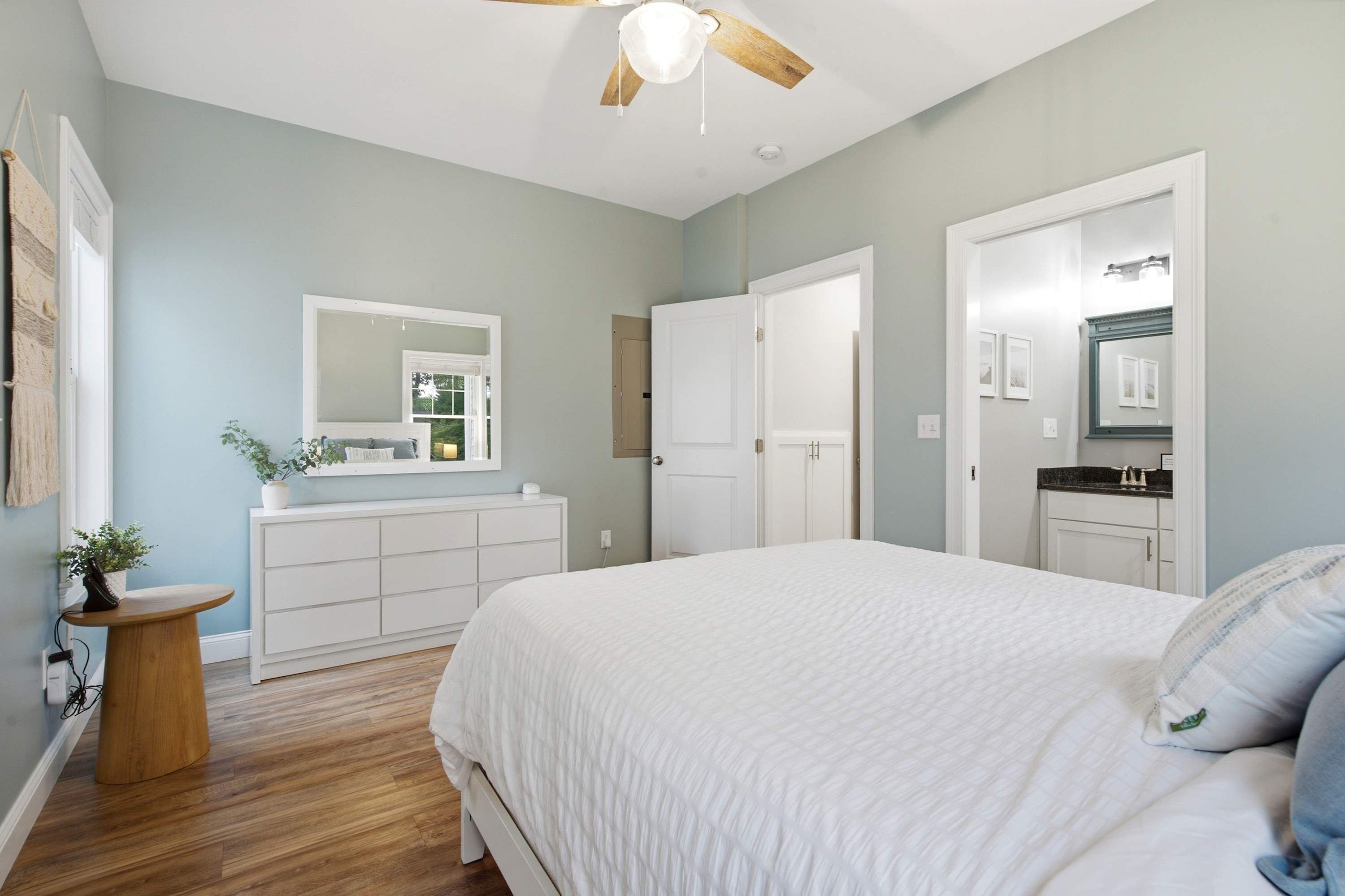 A bedroom with a bed, a dresser, a vanity with a mirror, and a ceiling fan.