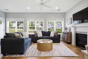 A living room with a dark grey sectional sofa, a round coffee table, and a fireplace. - Maritime Meadows Charming Resort-style Home! (Kennebunkport)