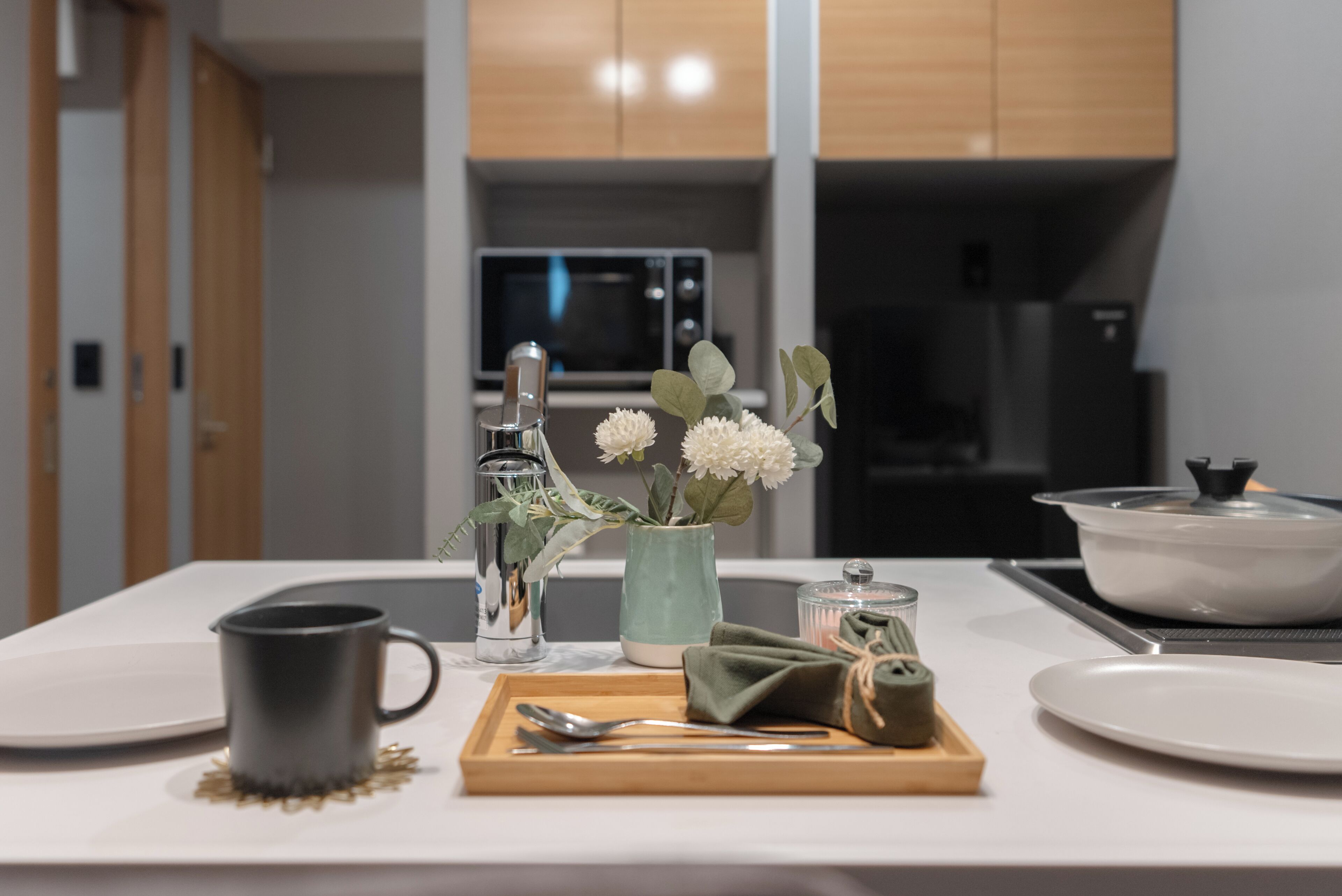 A modern kitchen with a microwave, stove, and a dining area set with a table, a vase with flowers, and a mug.