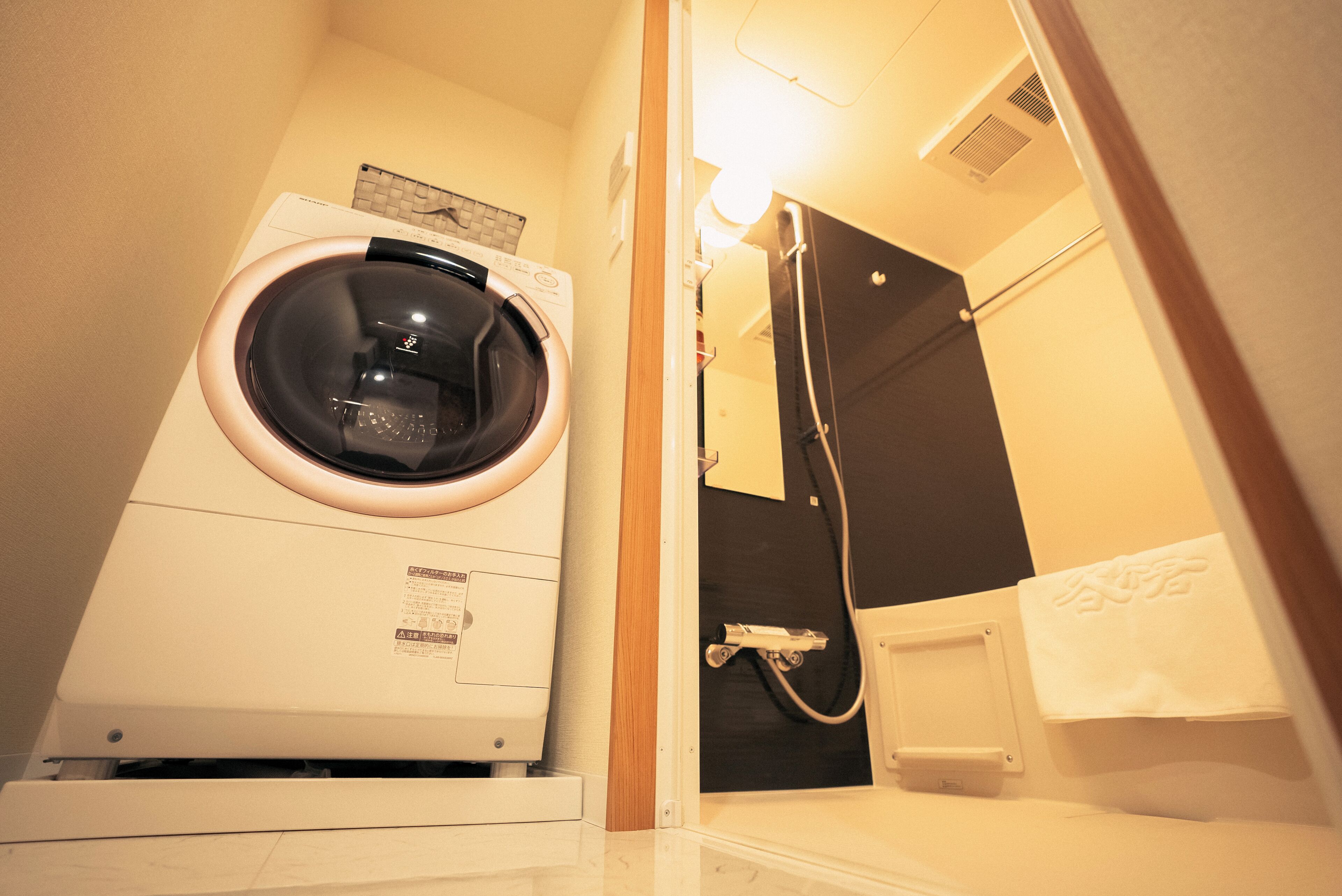 A compact hotel bathroom with a front-loading washing machine, a shower area, and a towel rack.