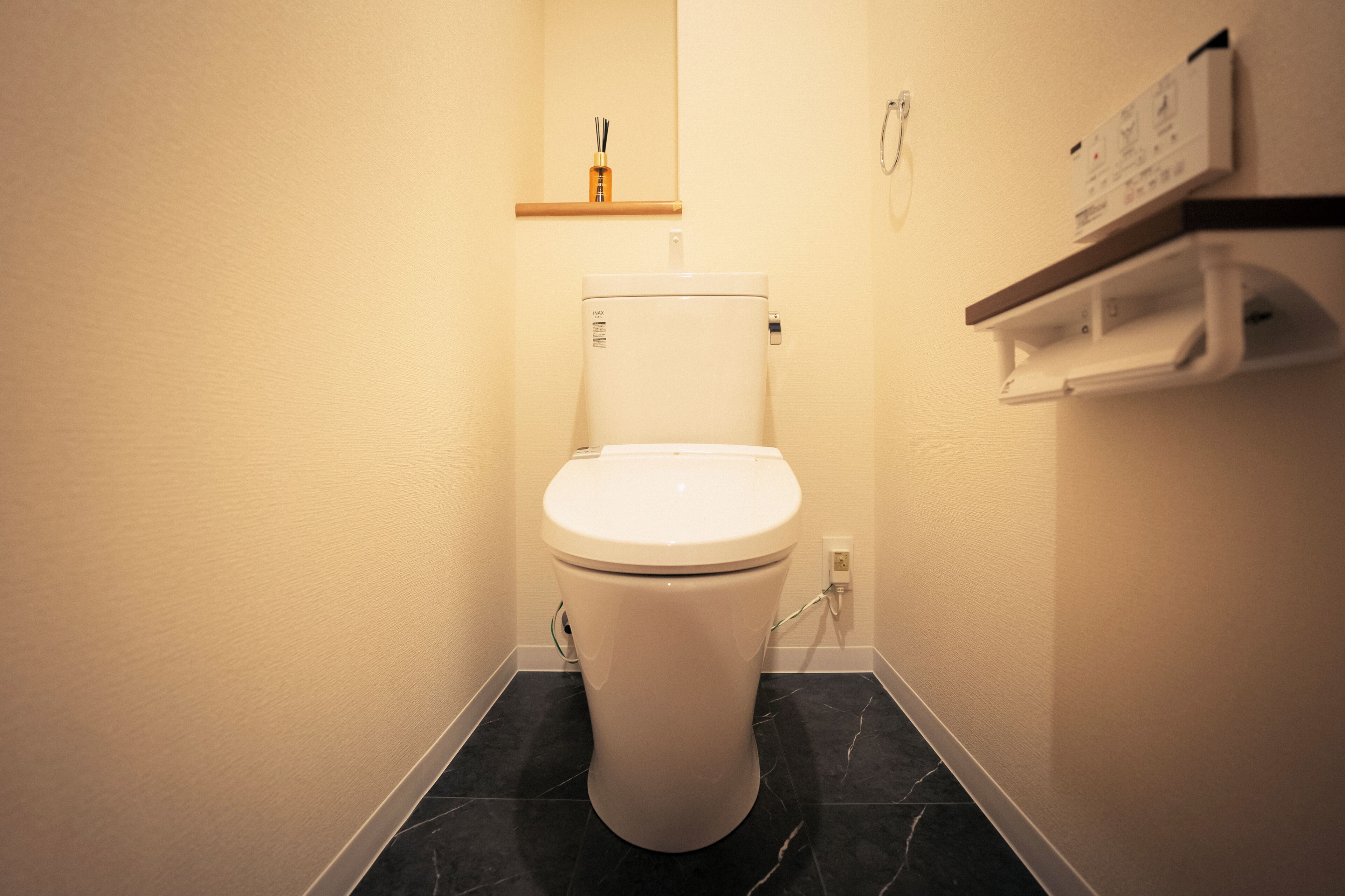 A white toilet with a marble floor, a wooden shelf above it, and a control panel on the wall.