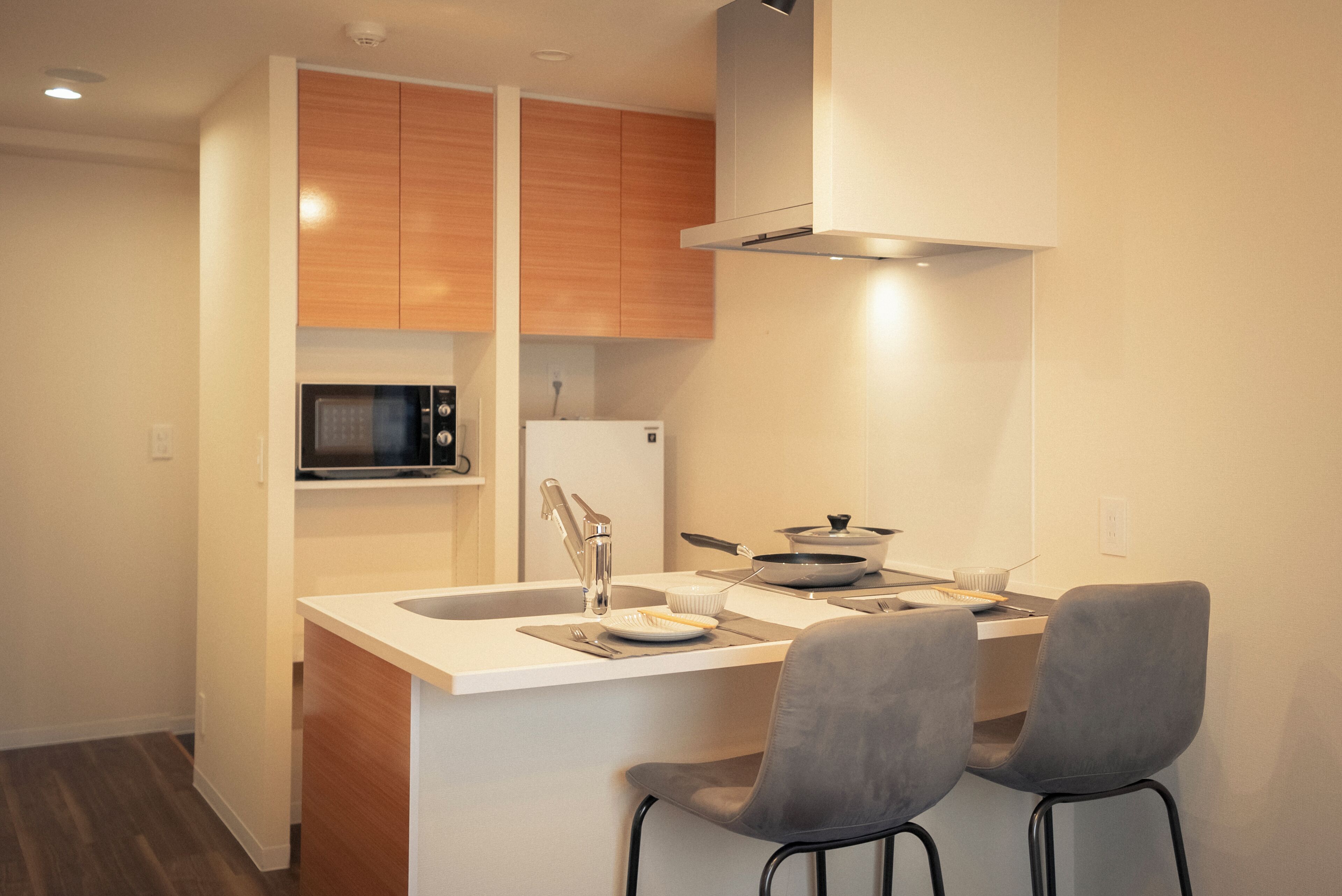A compact kitchen with wooden cabinets, a microwave, a refrigerator, and a small dining area with two chairs.