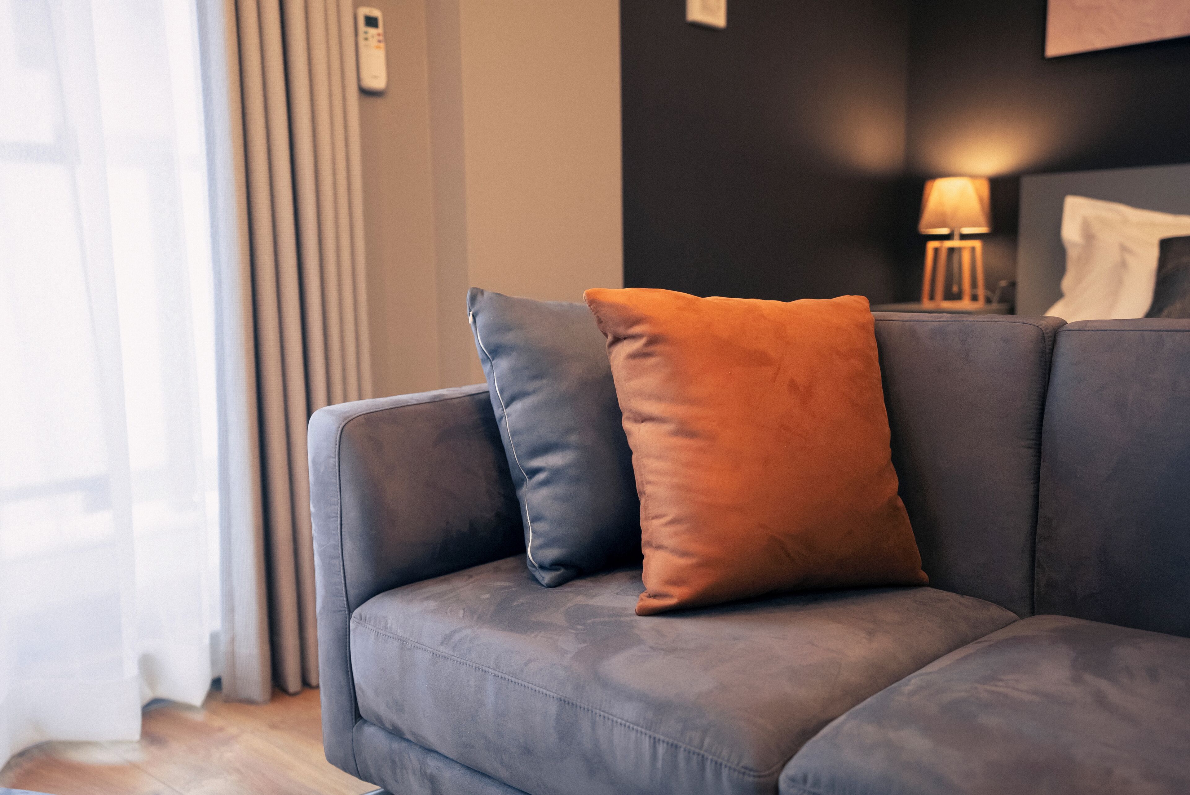 A grey sofa with two cushions, a lamp, and a remote control on a table.
