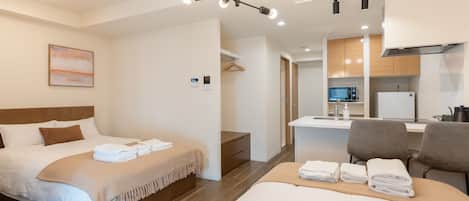 A hotel room with a bed, a desk, a chair, and a kitchenette.