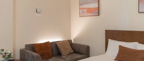 A hotel room with a bed, a sofa, a small table with a plant, and a painting on the wall.