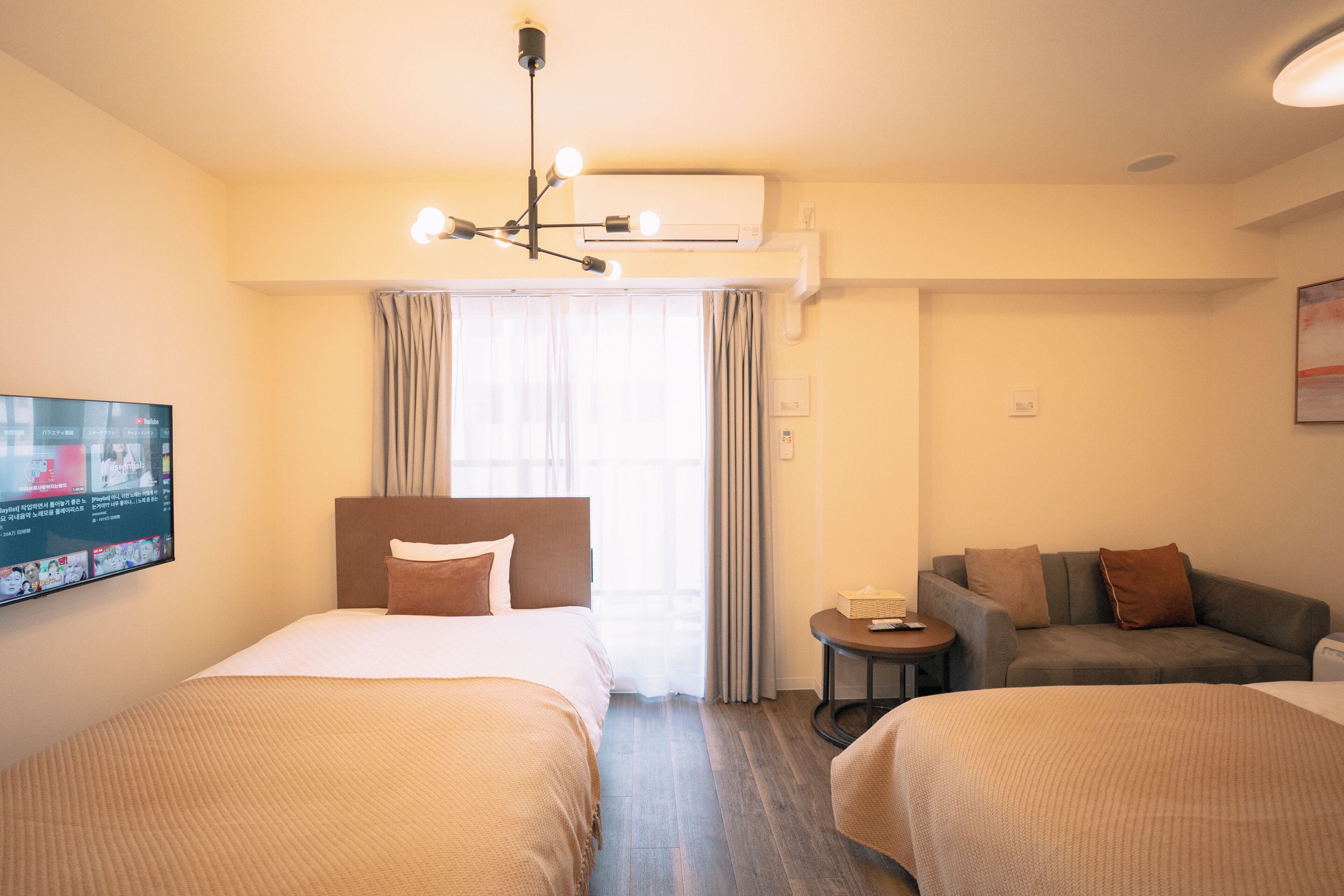 Une chambre d’hôtel avec deux lits, un canapé, une petite table et un téléviseur fixé au mur.
