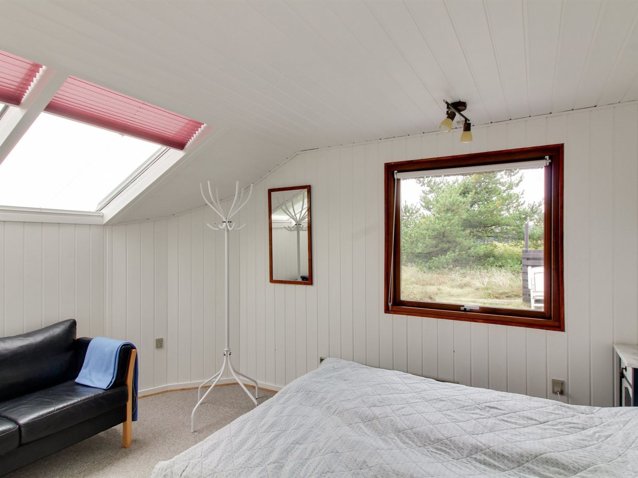Ein Schlafzimmer mit einem Bett, einem schwarzen Ledersofa, einer Stehlampe, einem Fenster und einem Dachfenster.