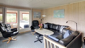 A modern living room with a black leather sofa, a round coffee table, and a black leather armchair. There are two windows with curtains, a painting on the wall, and a lamp on a side table. - "Kastehelmi" - 400m from the sea by Interhome (Blåvand)