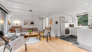 Un espacio moderno y abierto para sala y comedor, con piso de madera, paredes blancas y una cocina con gabinetes blancos y electrodomésticos de acero inoxidable.