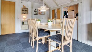 A dining area with a round table, four chairs, a hanging light fixture, and a kitchen visible through an open doorway. - "Emmi" - 2.5km from the sea by Interhome (Blåvand)