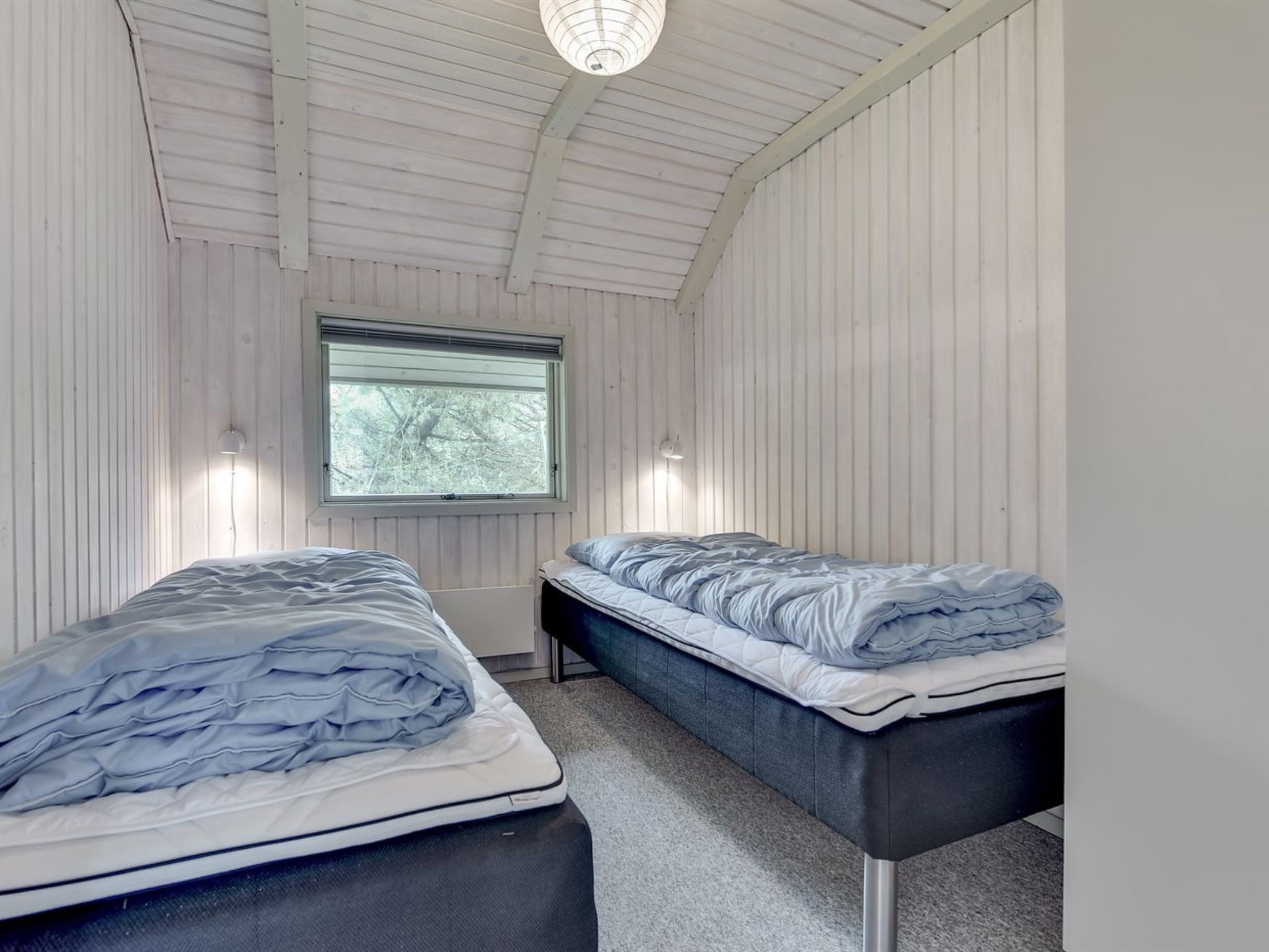Une chambre avec deux lits, une fenêtre et un luminaire au plafond.