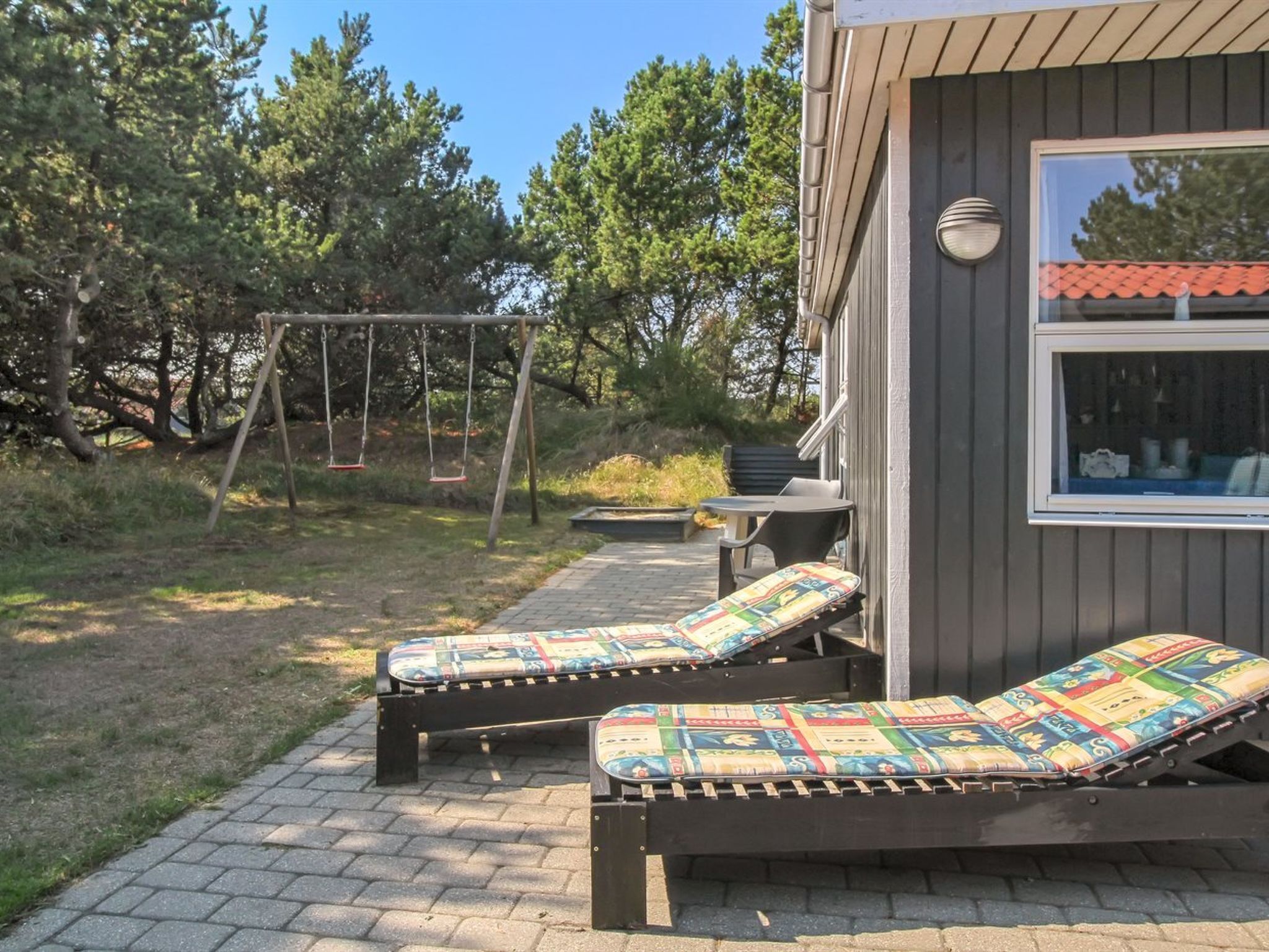 Une petite cabane avec deux fauteuils confortables à l’extérieur, une balançoire et un espace patio comprenant une table et des chaises.