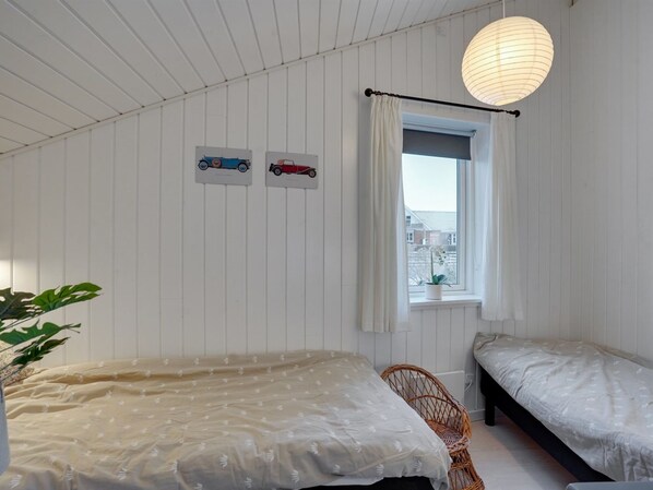 Un dormitorio con dos camas, una ventana con cortinas, una lámpara colgante y cuadros de autos en la pared.
