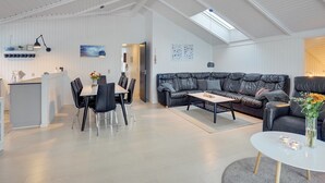 Un loft spacieux avec un plafond haut, un coin repas comprenant une table et des chaises, un canapé en cuir noir et une petite table ronde agrémentée d’un vase de fleurs.