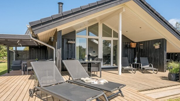 Une maison moderne dotée d’un patio couvert comprenant des chaises longues et une table.