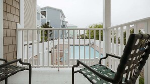 Un balcon avec deux chaises en métal, une clôture blanche et une piscine visible au fond.