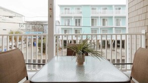 Un balcon avec une table et des chaises, un pot de fleurs et une vue sur un immeuble à plusieurs étages.