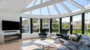 Ein modernes Wohnzimmer mit großem Fernseher, bequemen Sitzmöglichkeiten und einer Glaskuppel.