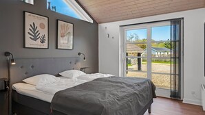 Ein Schlafzimmer mit Bett, Kopfstütze, Nachttisch, Wandbild und einem großen Fenster mit Blick.