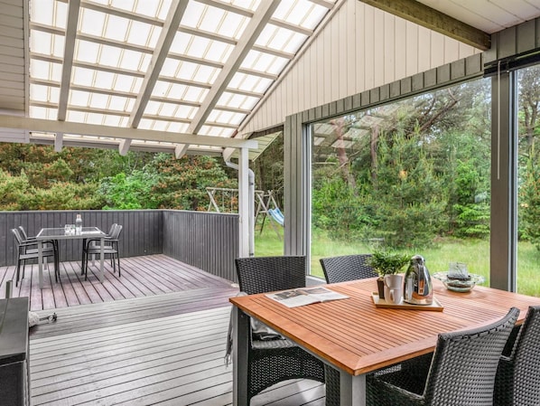 A covered patio with a table and chairs, a wooden deck, and a view of a garden.