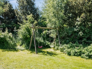 A wooden swing set in a lush garden with dense foliage and trees in the background. - "Femmy" - 600m from the sea by Interhome (Blåvand)