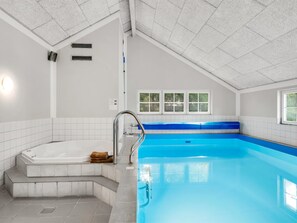Ein moderner, überdachter Pool mit Whirlpool, klarem blauen Wasser und einer schrägen Decke.