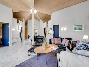 Ein geräumiger Wohnbereich mit hoher Decke, einem schwarzen Ledersofa, einem Couchtisch und Blick ins Freie.