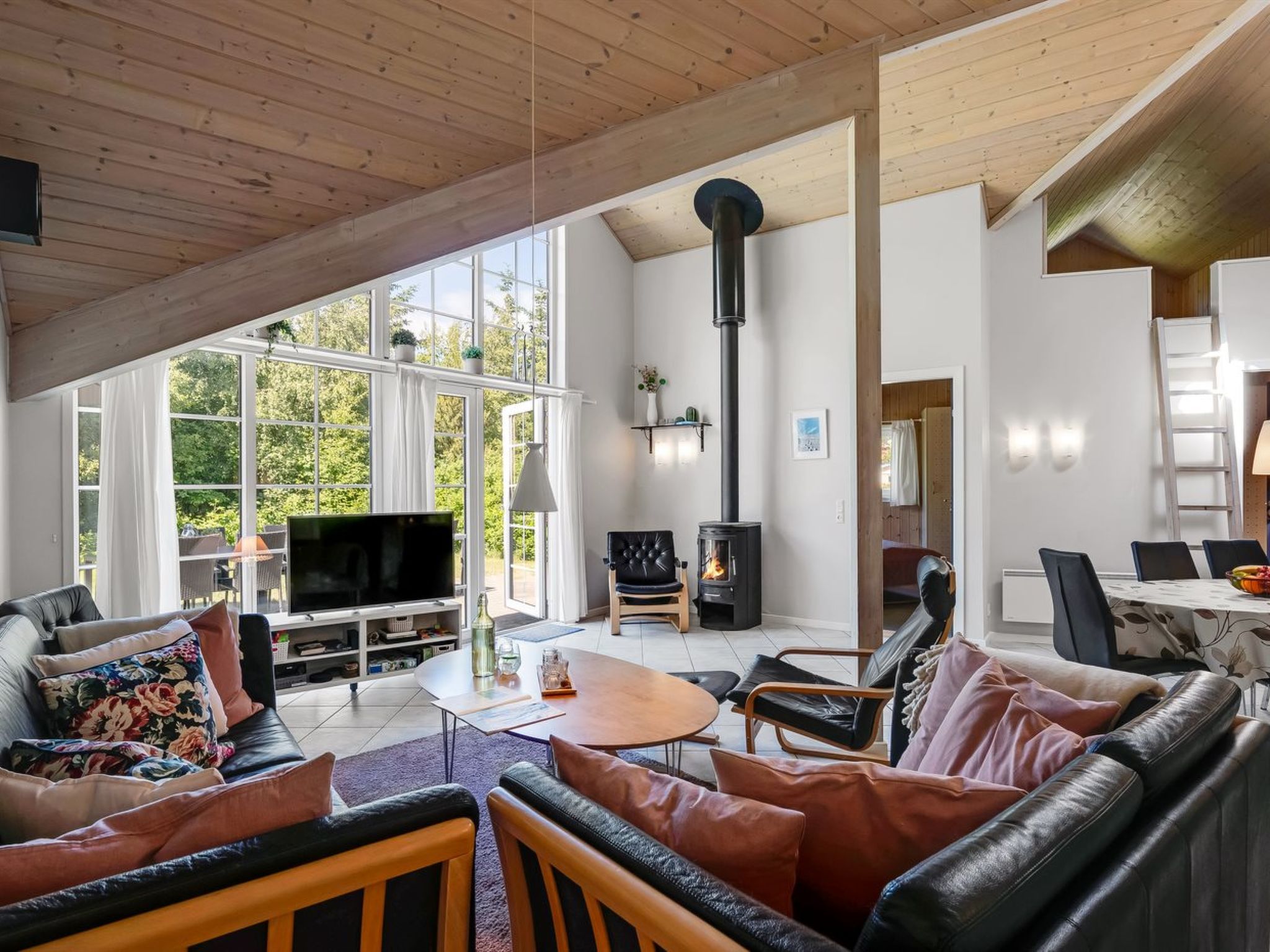 A spacious living area with a television, leather sofas, a fireplace, and large windows offering a view of greenery.