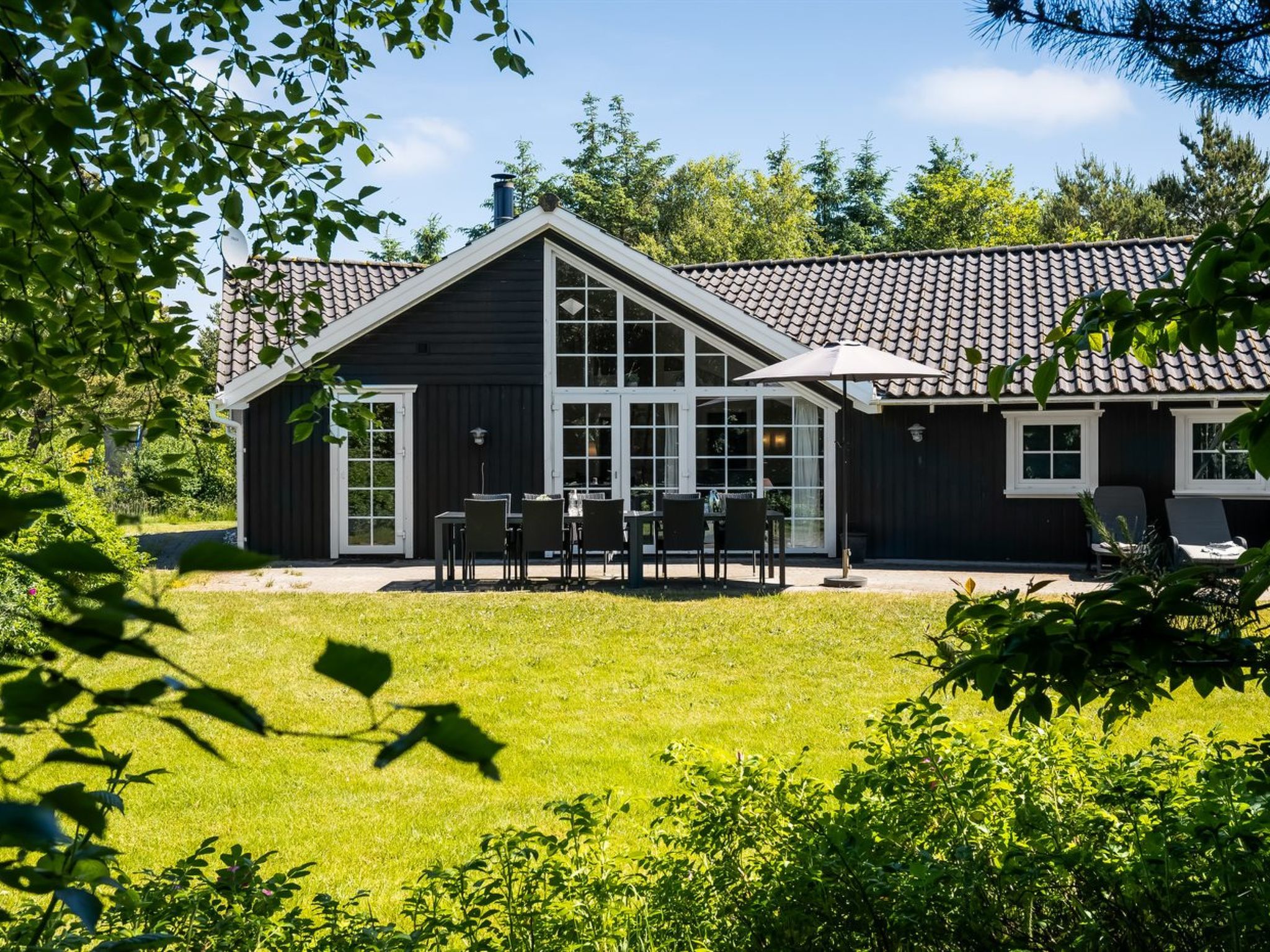 Ein zweigeschossiges Haus mit einer großen Veranda, einem Essbereich mit Sitzgelegenheiten im Freien und einem gepflegten Rasen.