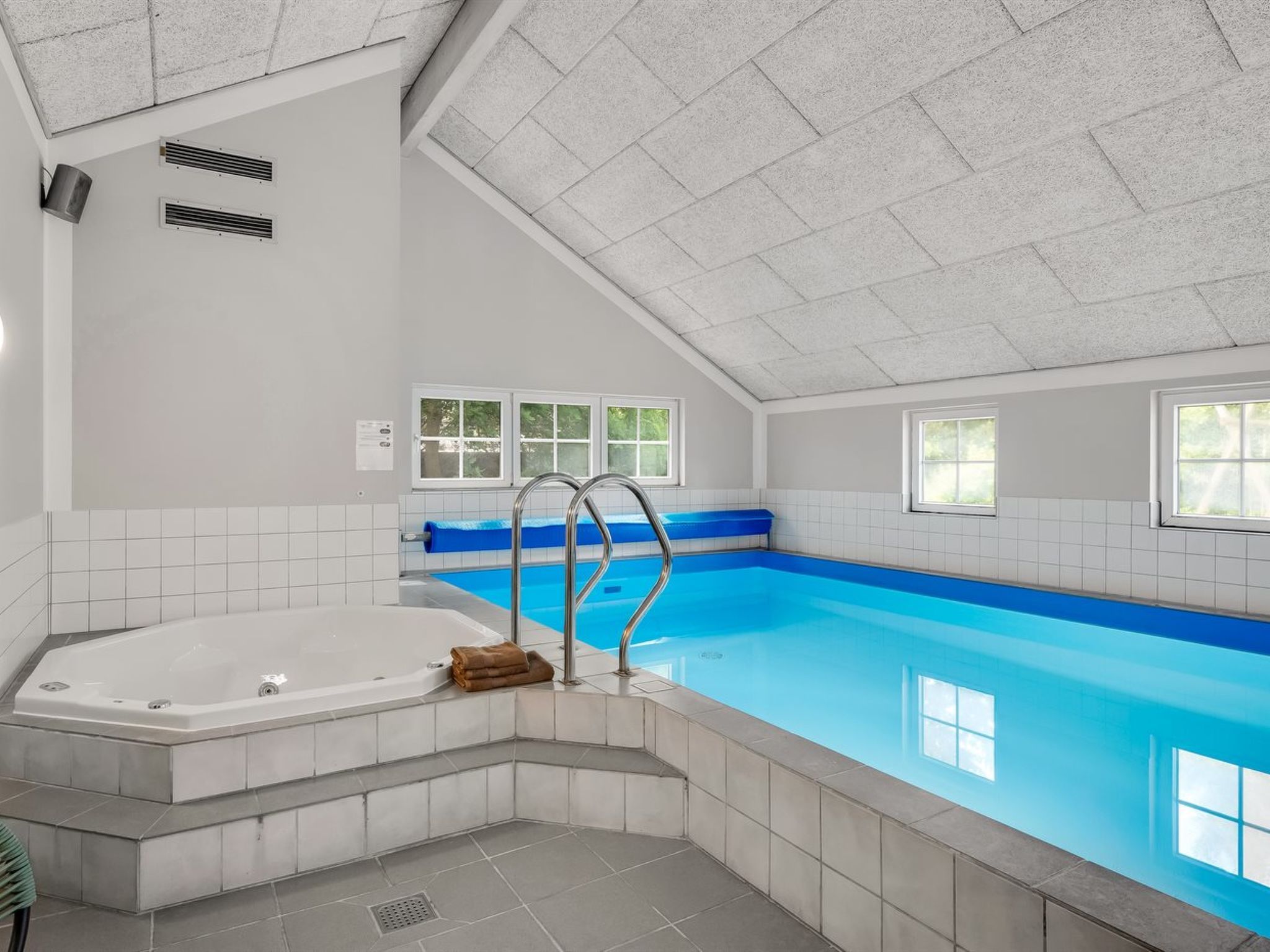 A swimming pool with a jacuzzi, tiled walls, and windows.