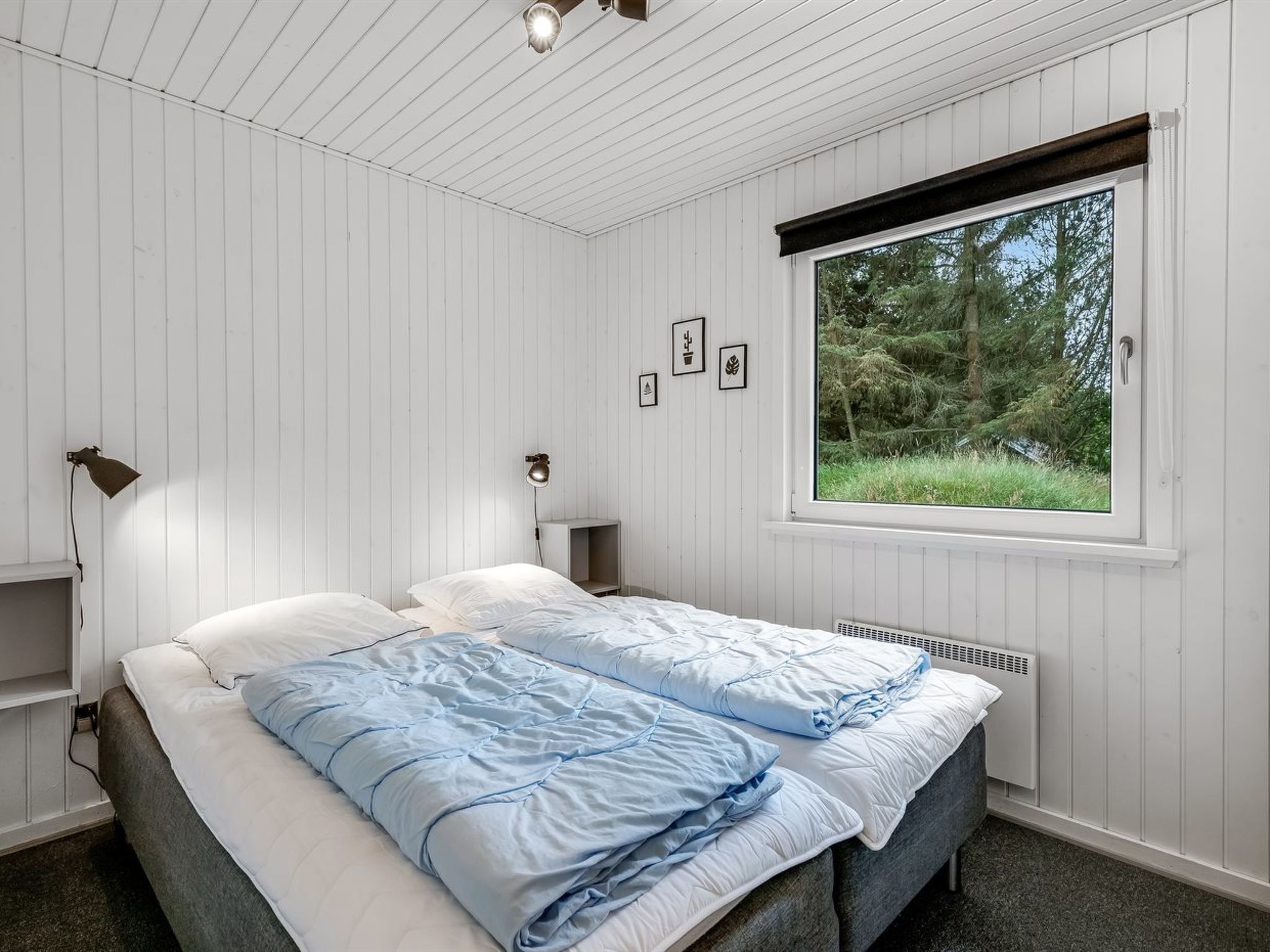 Ein Schlafzimmer mit einem Bett, einem Fenster mit Blick auf Bäume und einem Regal mit einer Lampe.