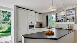 A modern kitchen with white cabinetry, a large island with fruit, pendant lighting, and a view of greenery outside. - "Raili" - 1.5km from the sea by Interhome (Blåvand)