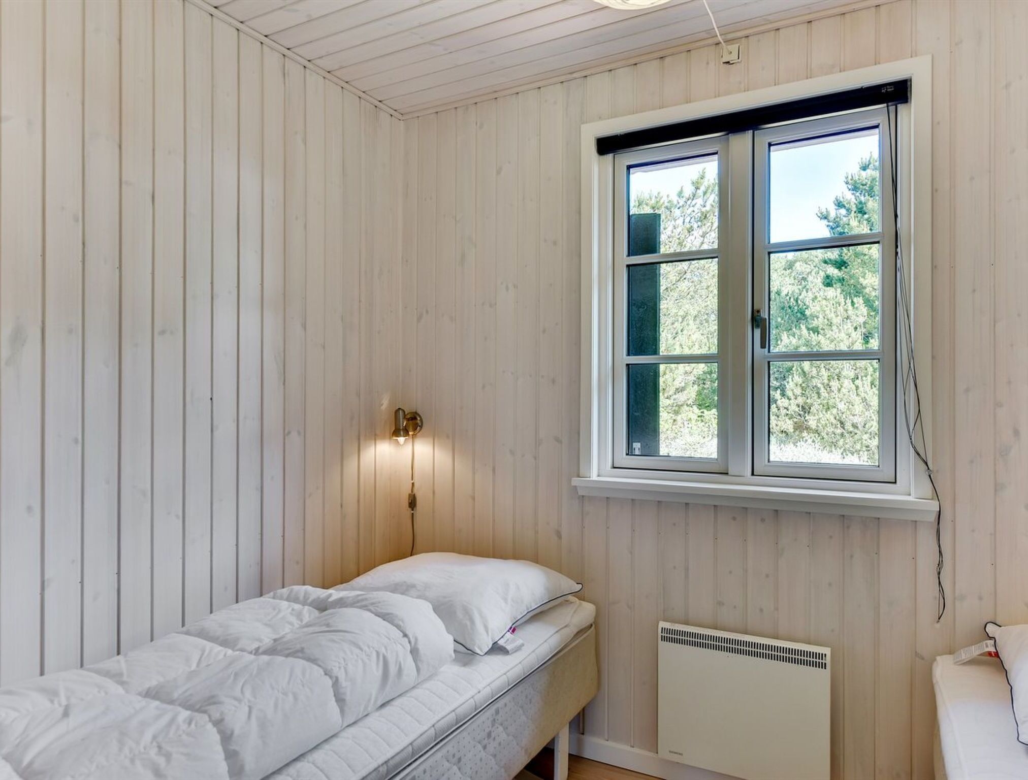 Een kamer met een enkel bed, een raam met uitzicht op bomen, en een wandradiator.