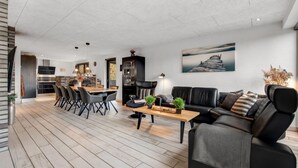 A modern living room with a black leather sofa, a wooden coffee table, and a dining area with a brick wall and black chairs.