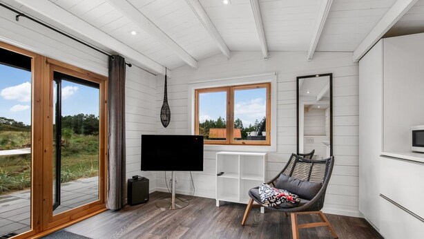 A modern room with a large window, a flat-screen TV, a wooden floor, and a chair with a cushion.
