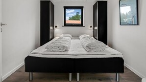 A modern bedroom with a bed, a window, and a ceiling light.