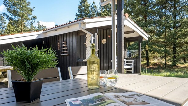A wooden table with a potted plant, a bottle, glasses, and a newspaper.