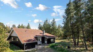 A cabin with a sloped roof, a porch, and a gravel driveway surrounded by trees.
