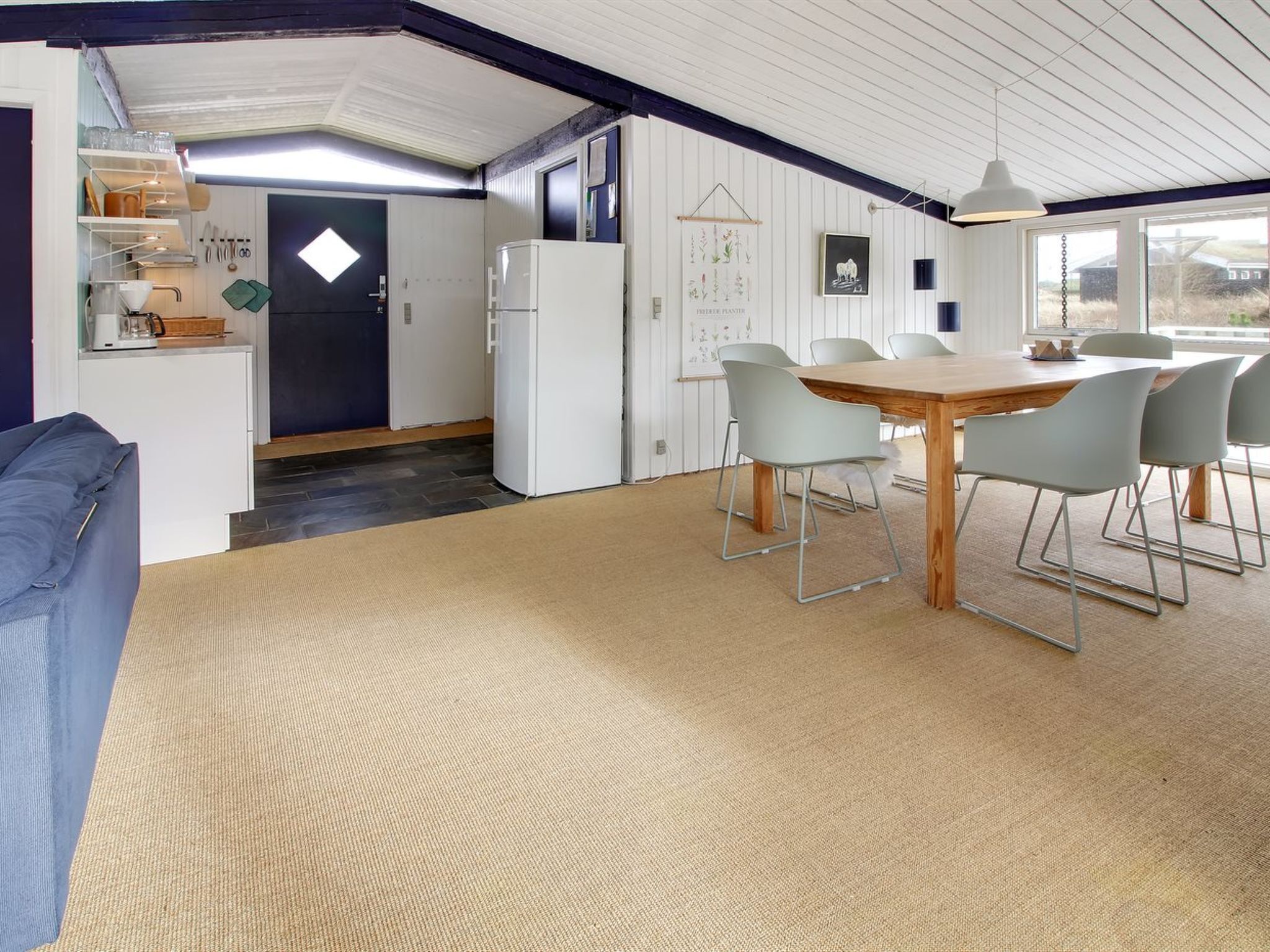 A modern kitchen with white cabinets, a refrigerator, and a dining area with a wooden table and four chairs.
