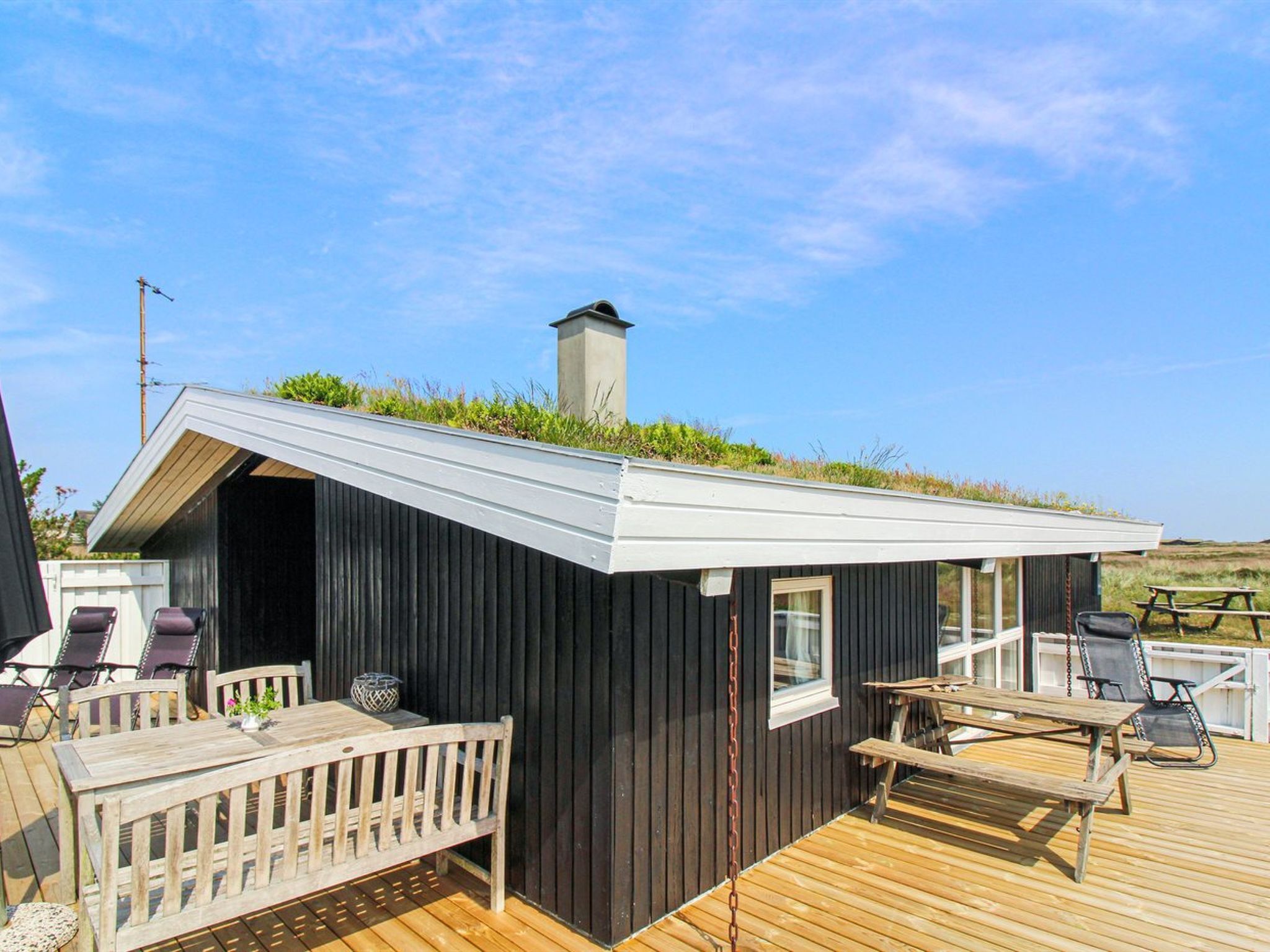 A small wooden cabin with a sloped roof, a deck with seating, and a chimney.