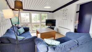 Ein gemütliches Wohnzimmer mit zwei blauen Sofas, einem Holztisch, einer Stehlampe und einem Fernseher.