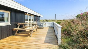 Eine Holzterrasse mit Picknicktisch und Stühlen, eine kleine Sitzgruppe im Freien und Blick auf die umliegende Landschaft.