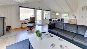Un salón amplio con techo alto, un sofá de cuero negro, una mesa de centro blanca y una mesa de comedor para seis personas.