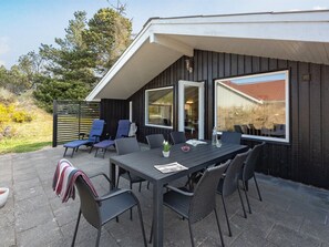 Un patio al aire libre con una mesa y sillas, un área de estar cubierta y ventanas grandes.