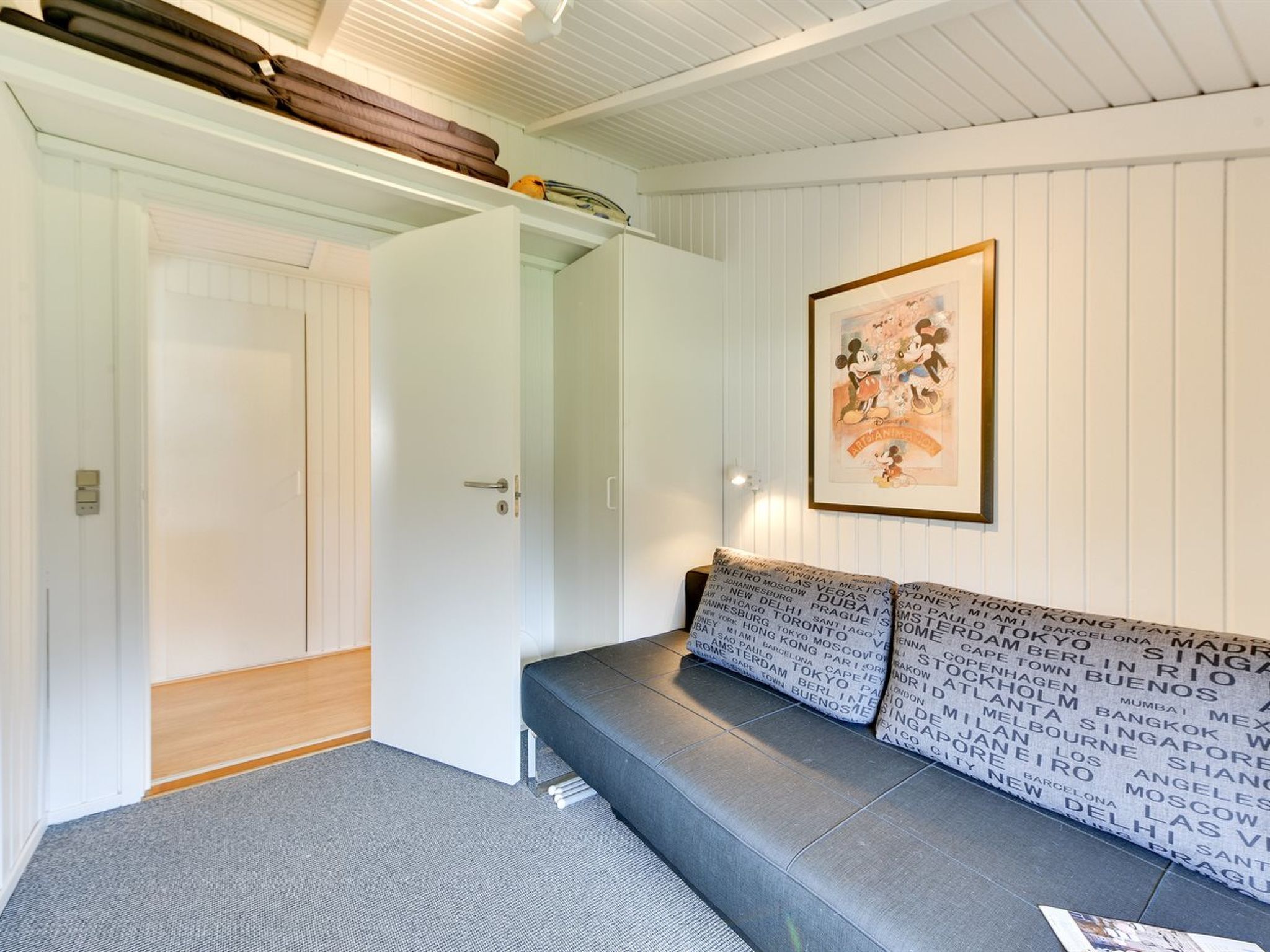 A room with a grey sofa, a framed picture on the wall, and a white wardrobe with a door open.